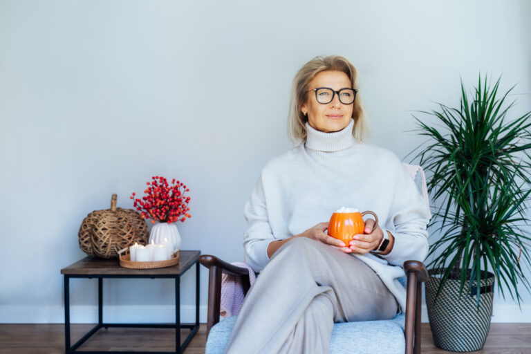 Woman relaxing with a bold orange cup of hot drink in scandy style hygge interior home with a nurturing decor. Lady dreaming, enjoy calm mood without stress, well being alone.